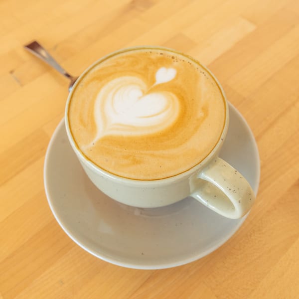 Latte art with a heart design in a light-colored mug on a saucer, on a wooden table.