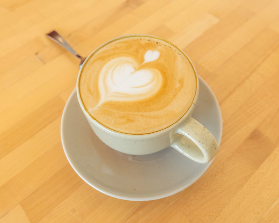Latte art with a heart design in a light-colored mug on a saucer, on a wooden table.