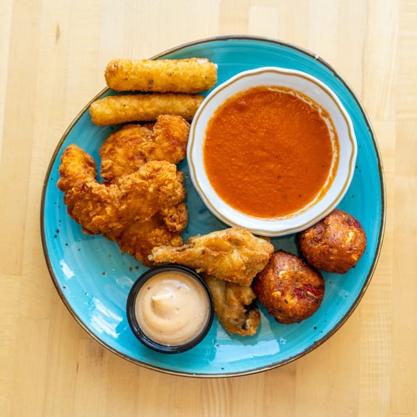 A blue plate with fried chicken, mozzarella sticks, hush puppies, and two dipping sauces.
