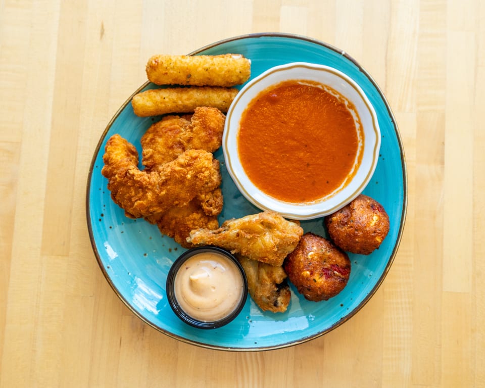 A blue plate with fried chicken, mozzarella sticks, hush puppies, and two dipping sauces.