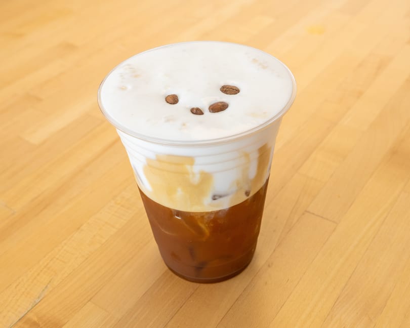 Iced coffee with a thick layer of cream and three coffee beans on top, on a wooden table.