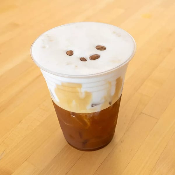 Iced coffee with a thick layer of white foam and three coffee beans on top.