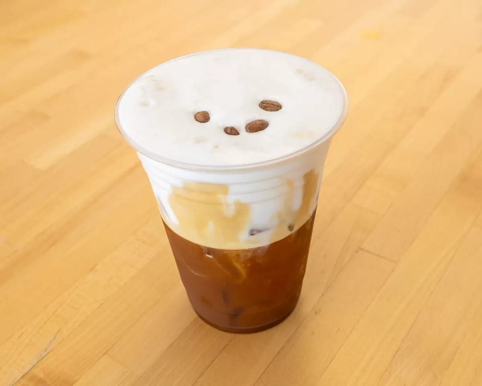 Iced coffee with a thick layer of white foam and three coffee beans on top.