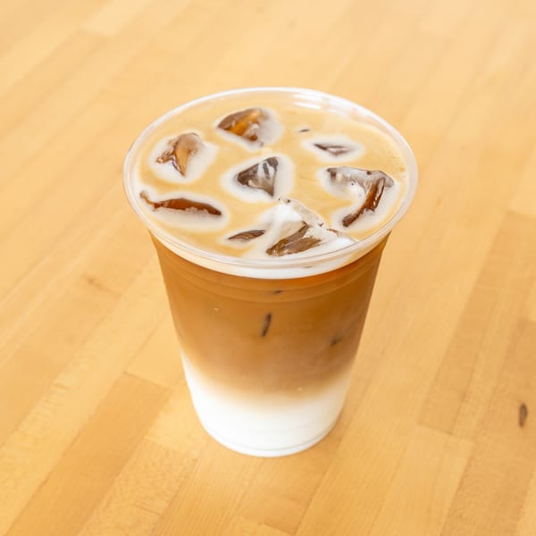 Iced latte with distinct layers of milk and coffee, topped with ice cubes, on a light wooden surface.