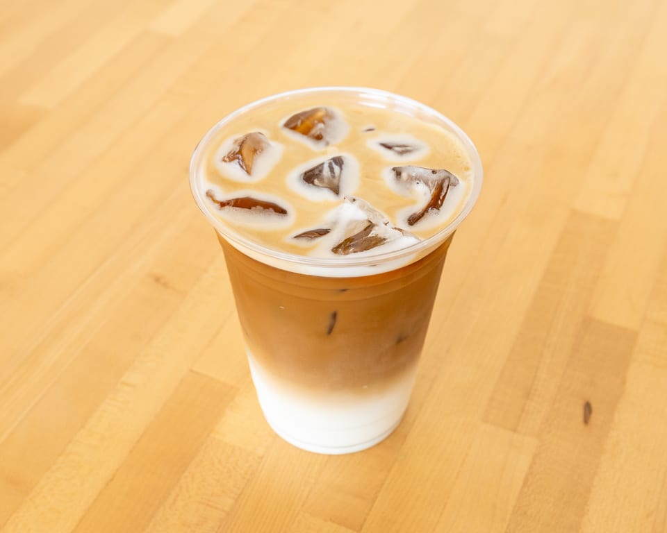 Iced latte with distinct layers of milk and coffee, topped with ice cubes, on a light wooden surface.