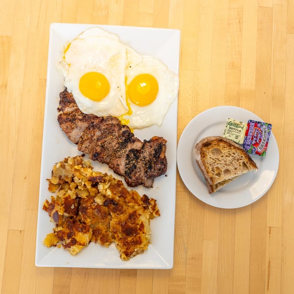 Steak and eggs breakfast with hash browns, toast, butter, and jelly on a wooden table.