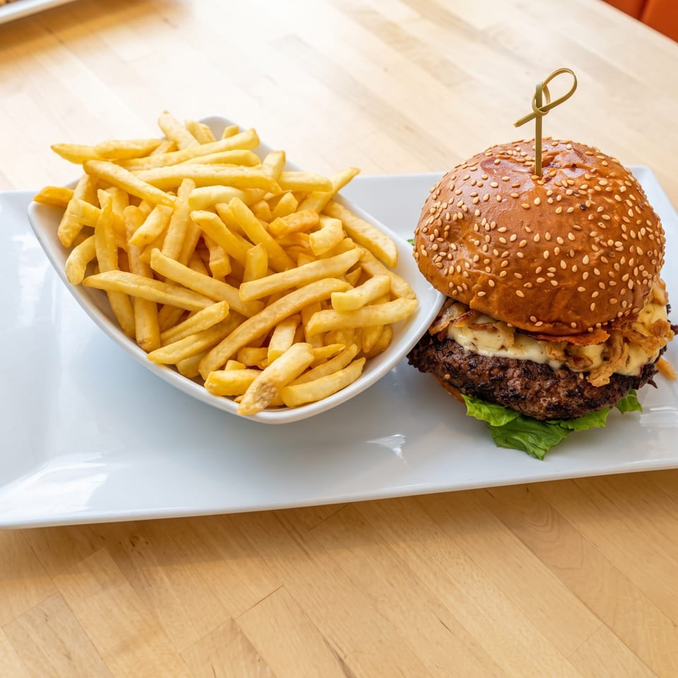 Sesame-seed cheeseburger with lettuce and crispy toppings served alongside golden fries on a white plate.