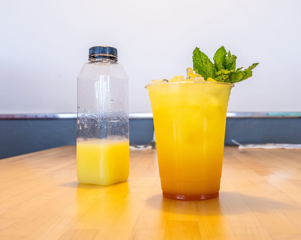 A plastic bottle with yellow liquid and a cup of iced yellow drink with mint on a wooden table.