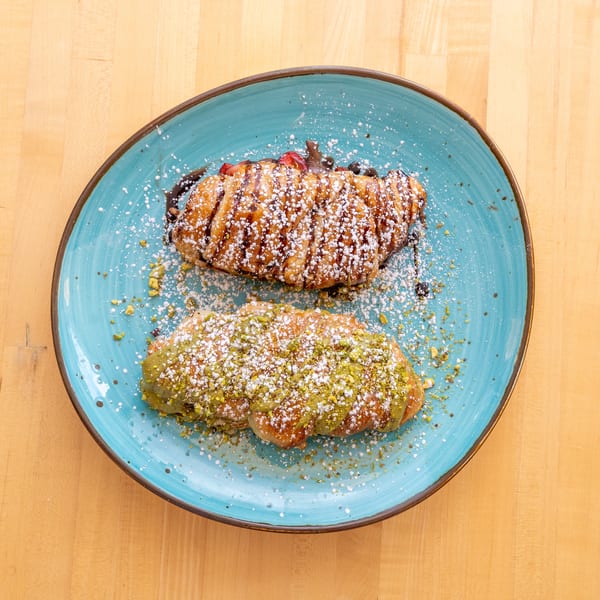 Two croissants, one with chocolate and strawberries, the other with pistachio, on a blue plate.