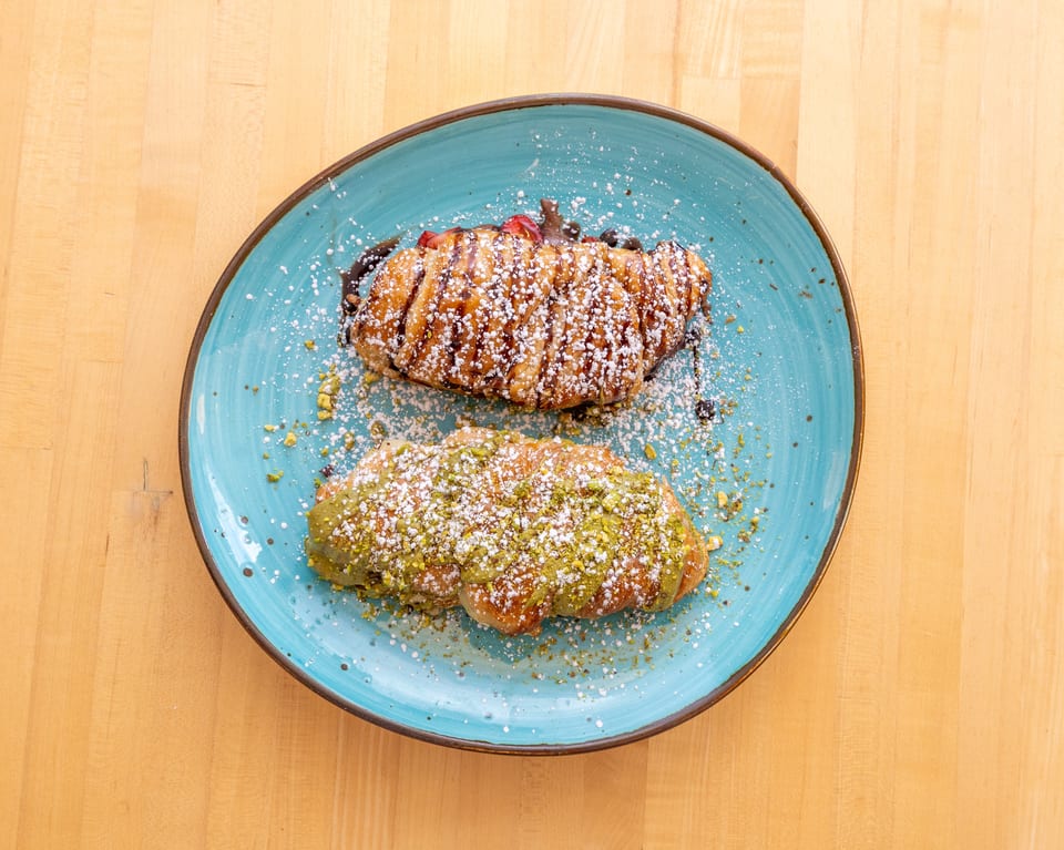 Two croissants, one with chocolate and strawberries, the other with pistachio, on a blue plate.