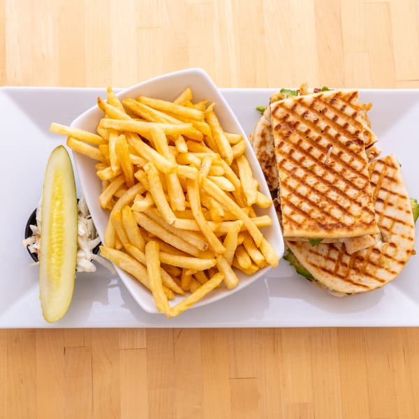 Grilled quesadilla with chicken and avocado, served with a side of french fries, coleslaw, and a pickle.