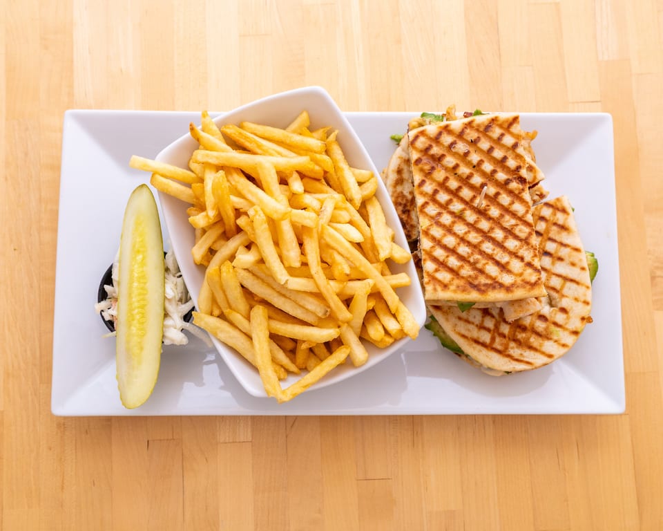 Grilled quesadilla with chicken and avocado, served with a side of french fries, coleslaw, and a pickle.