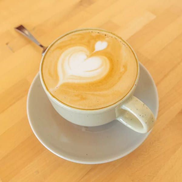 Latte art with a heart design in a white cup on a saucer, on a wooden table.